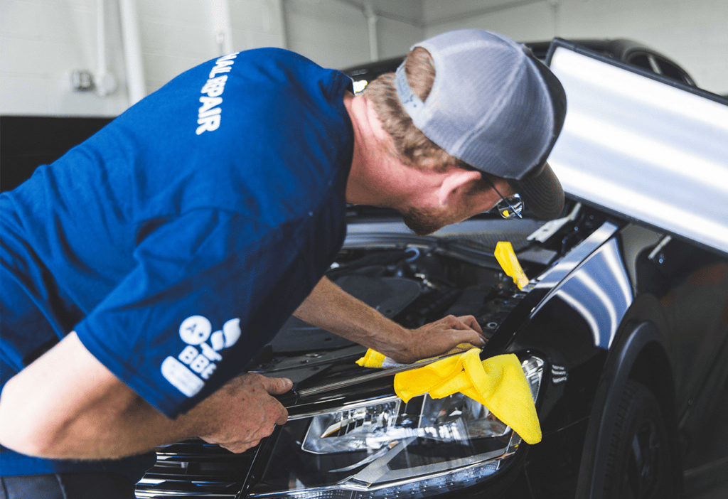 man performing paintless dent repair on black car